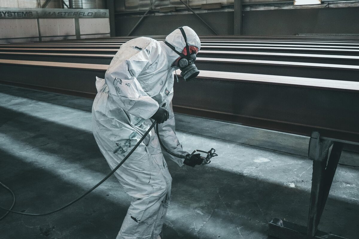 Industrial painter in full PPE spray painting steel beams