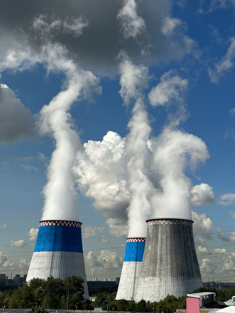 Three large industrial cooling towers releasing steam against a bright blue sky at a power plant