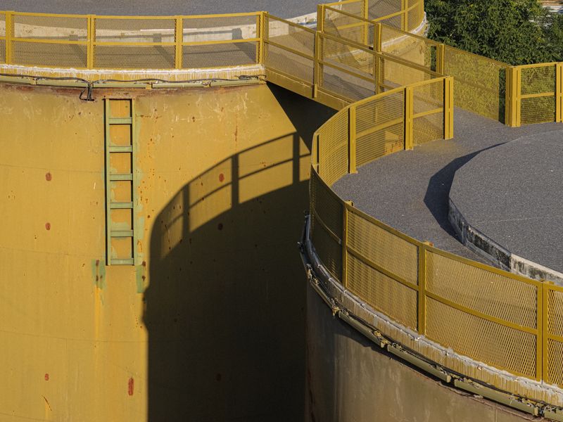 Large industrial oil storage tank with yellow safety railings and ladder at a chemical storage facility