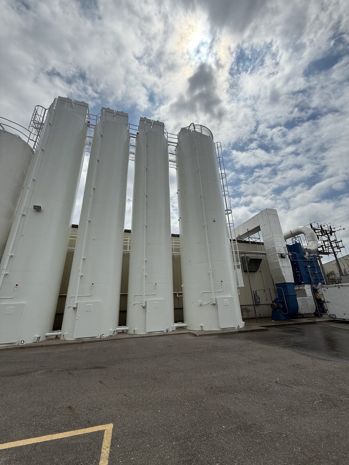 Four tall white industrial storage silos against a dramatic cloudy sky