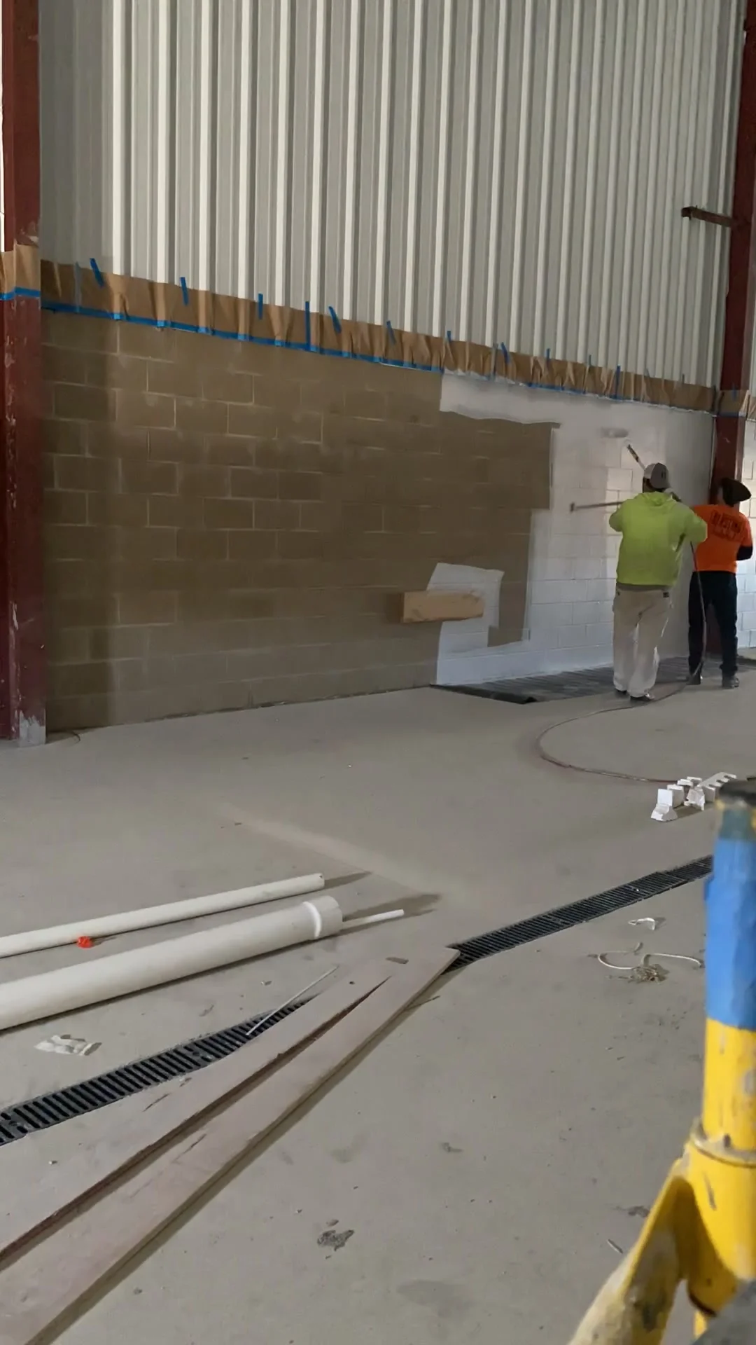 Crew starting block fill application — two painters rolling thick filler into the lower CMU wall sections