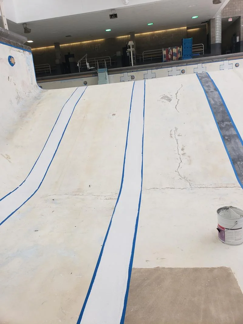 Pool surface prepped for recoating, worn concrete with lane guides taped off
