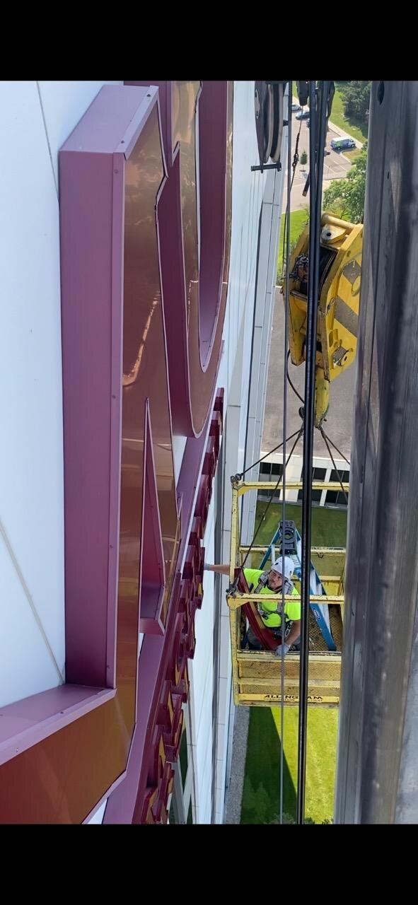 Painter in crane basket at height — sign repaint on 200-foot CMU building