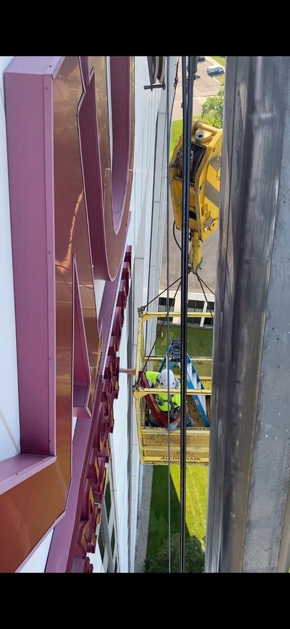 Painter working at height in crane basket — applying finish coat to exterior sign panel
