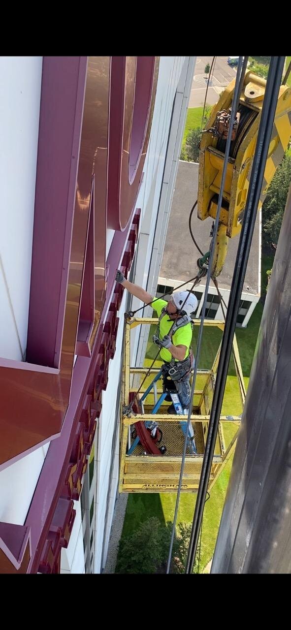 Full building view — crane positioned against 200-foot CMU exterior during sign repaint