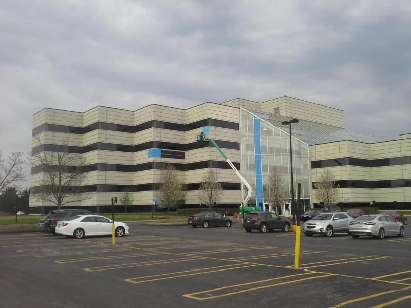 Multi-story office building exterior with an aerial lift working on the upper-floor facade