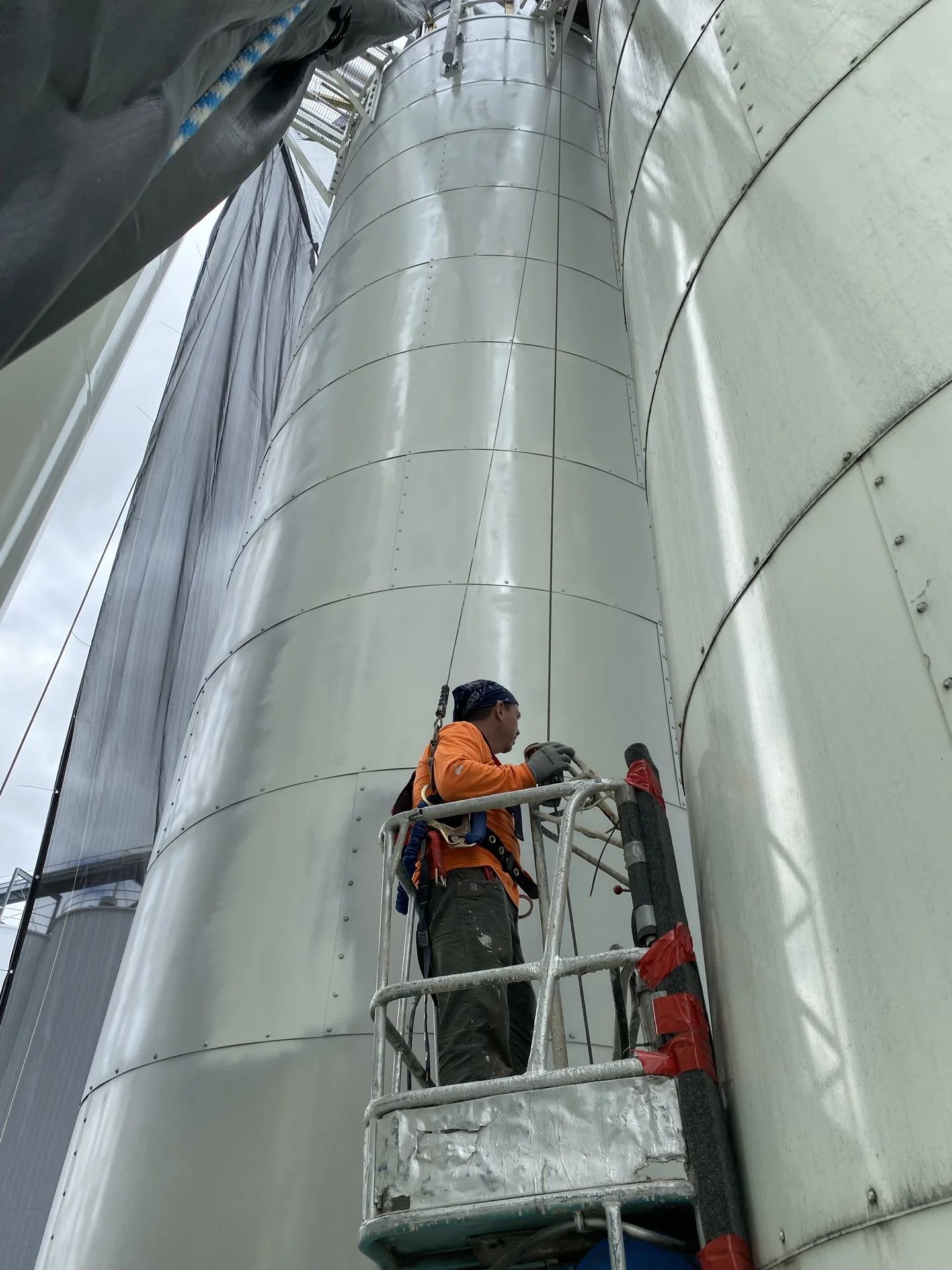 Endurance Painting crew member on suspended platform, coating the exterior of a tall grain silo