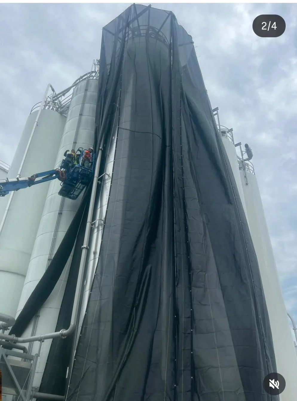 Full containment system deployed — black tarps draped over a tall silo with crew on aerial lift visible