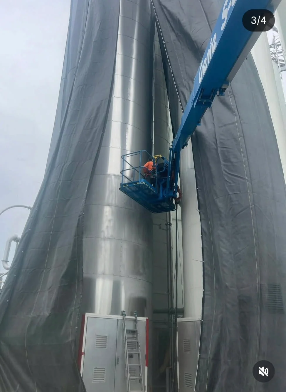 Crew on boom lift with full black containment tarps deployed around a silo during blasting operations