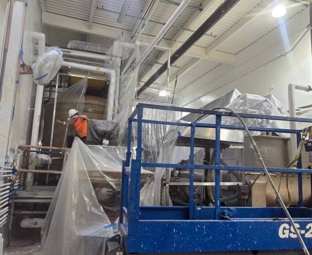 Crew on aerial lift applying paint to upper walls